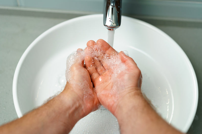Hombre adulto quitándose el jabón de las manos bajo el grifo de agua
